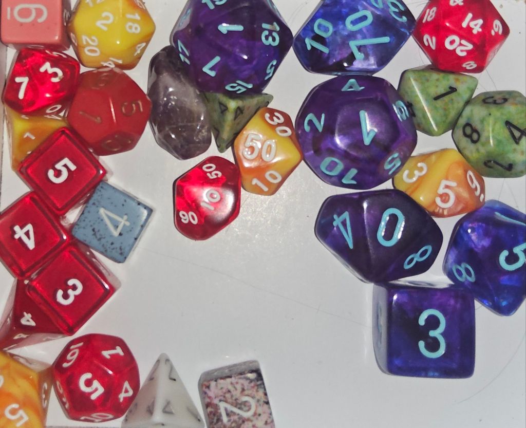 Assorted polyhedral dice. Assorted colors, sizes and side counts.  Gaming dice.  An amethyst crystal snuggled in between some dice. 