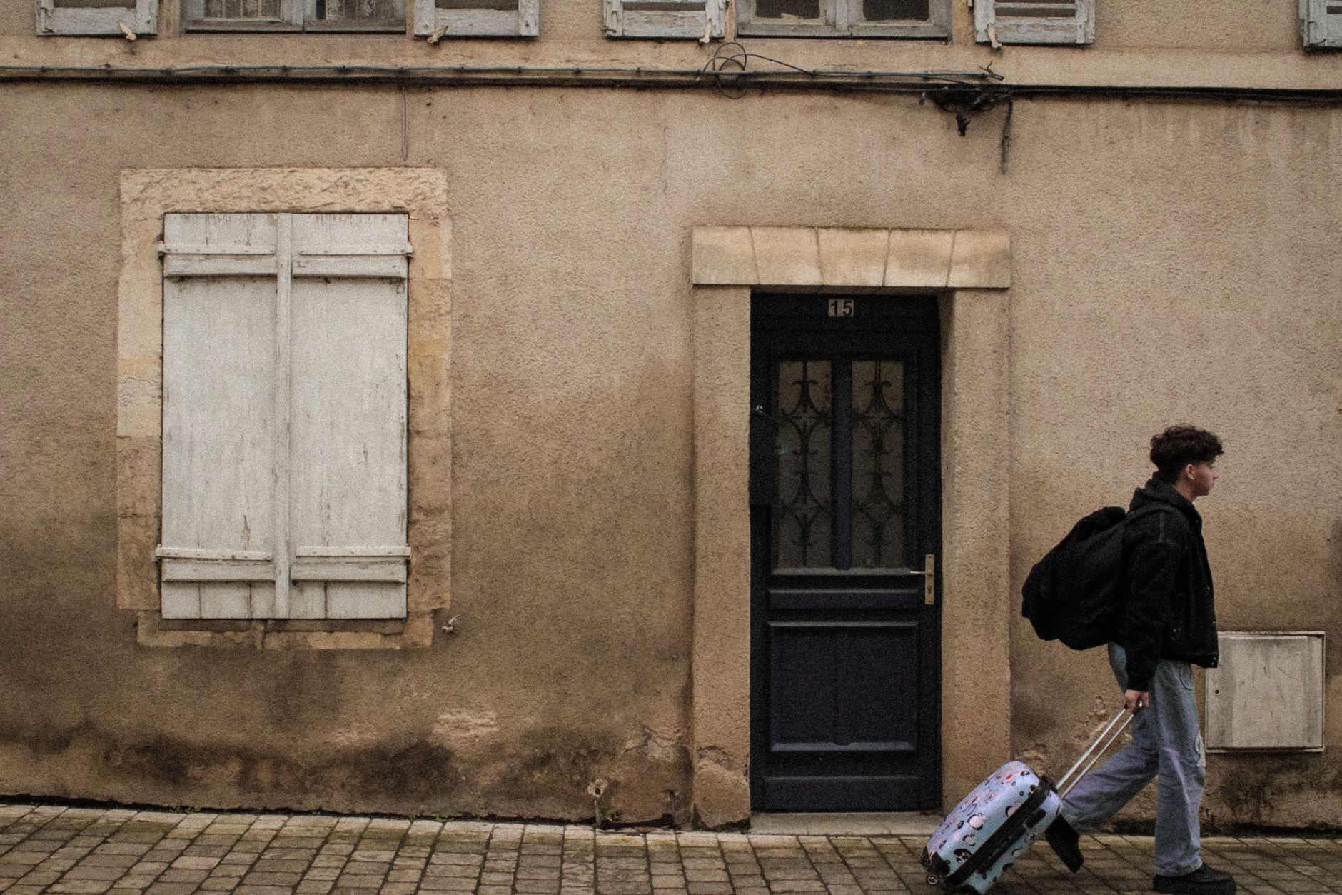Pearson with luggage walking past a door. Window is shuttered.