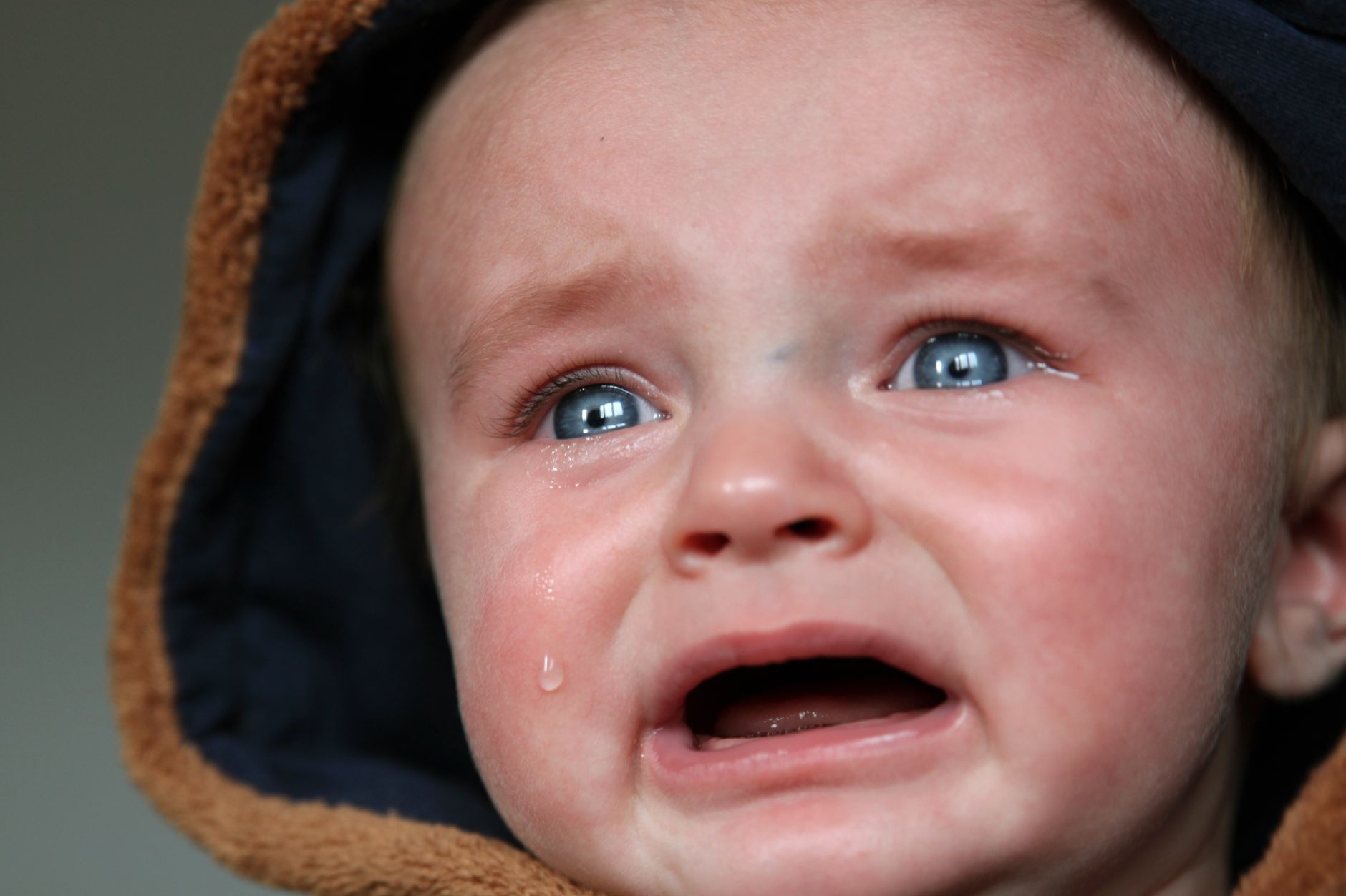 Baby crying with tears on cheek.